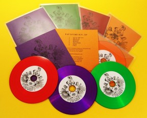 Red, green, orange and purple vinyl CDs in clear wallets with metallic card inserts