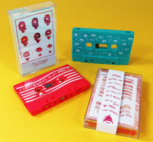 Neon pink and turquoise cassette shells with white on-body UV LED printing, packed in cases with obi strips