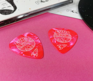 Pink guitar picks with a single colour cream print for Luna and the Moonhounds