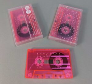 Transparent pink cassette tapes with white on-body printing, packed in clear frosted cases also with white on-body printing